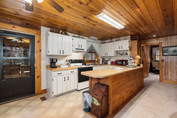 A kitchen with wooden cabinets, a central island, and a black stove. - ROCKY TOP LOG CABIN-PET FRIENDLY (MAGGIE VALLEY)