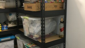 A storage area with shelves holding various items including boxes, plastic containers, and a bottle.