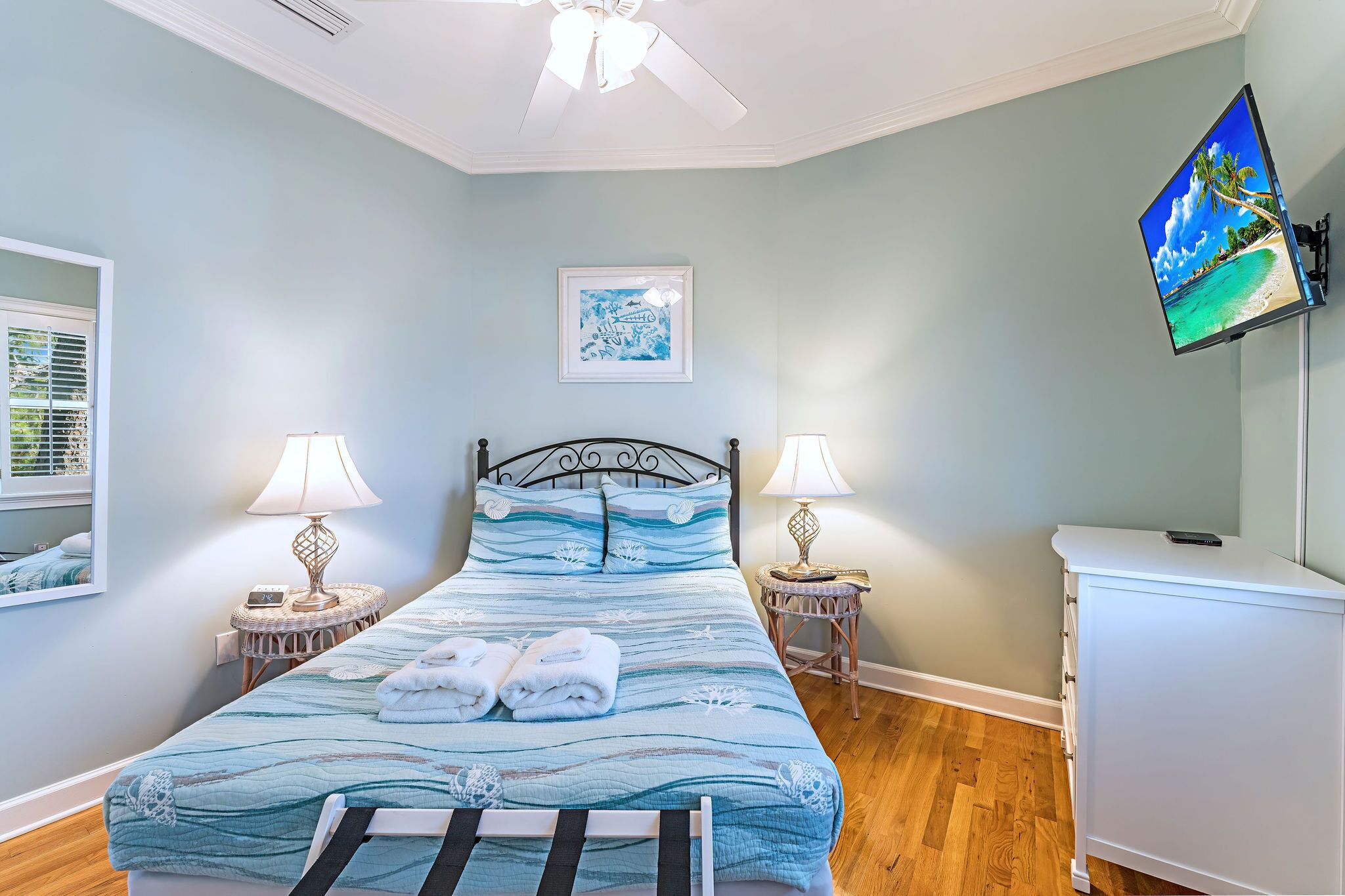 A bedroom with a bed, two bedside tables with lamps, a ceiling fan, a TV on the wall, and a framed picture on the wall.