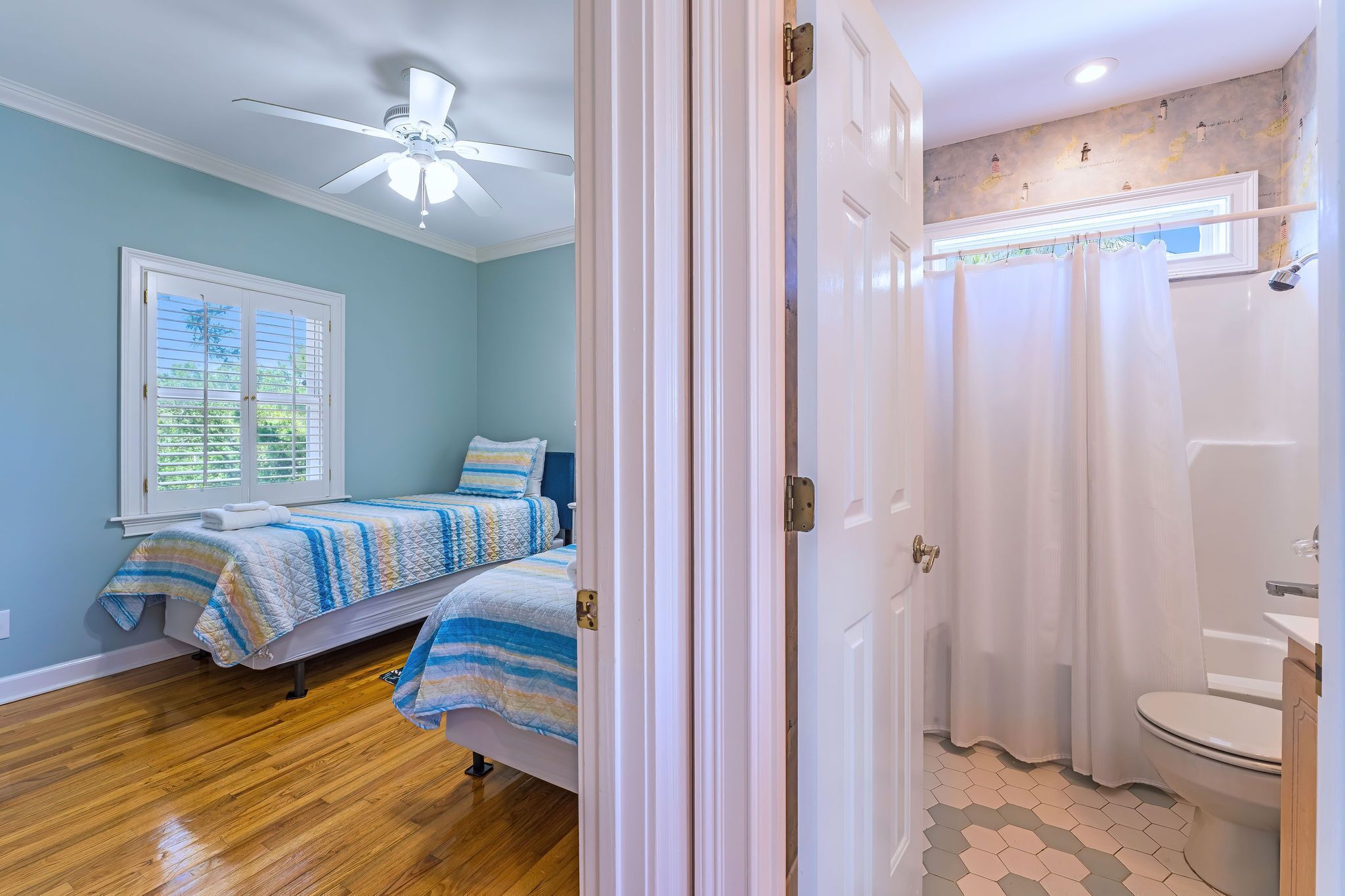 Une chambre à coucher avec un lit, un ventilateur de plafond, une fenêtre et une salle de bain avec un rideau de douche.