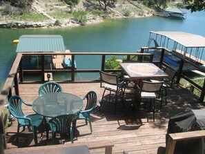 A wooden deck with a table and chairs, overlooking a calm body of water. - 5 bedroom/4 bath TH, with private boat dock on Lake Travis in Point Venture (Point Venture)