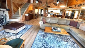 Un intérieur de chalet chaleureux avec un escalier en bois, un coin salon doté d’un canapé et d’un pouf, une table à manger et une cheminée.