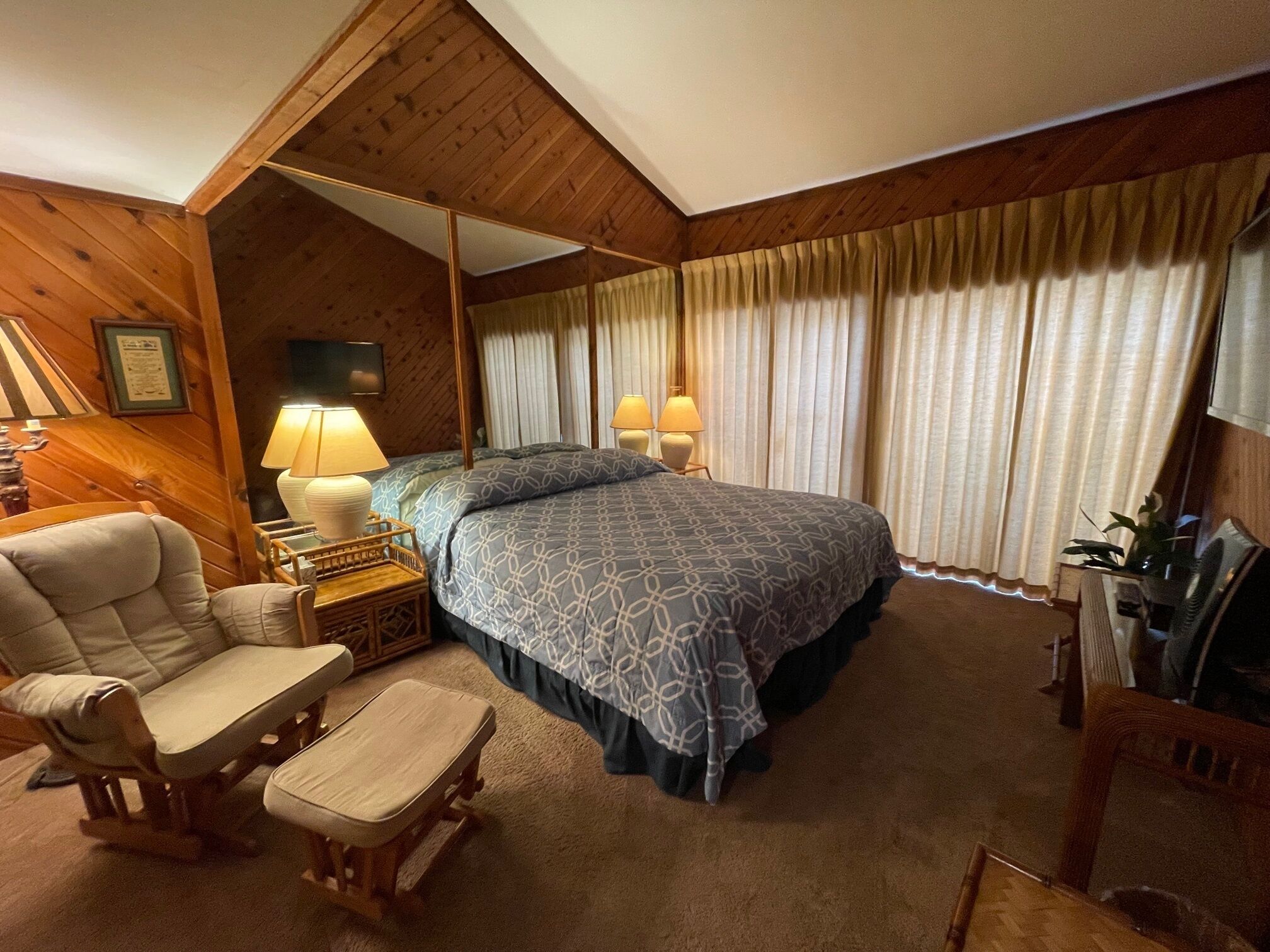 A cozy room with a large bed, two bedside lamps, a wooden chair, a small table, and a television.