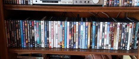 A bookshelf filled with DVDs and a stack of audio equipment.