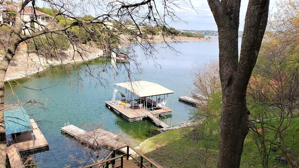 Une terrasse au bord du lac avec une table et des chaises, un espace salon couvert et un quai avec un bateau.