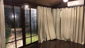Ein Zimmer mit einem großen Schiebeglasfenster, das in einen Garten führt, Holzboden und einer Decken-Klimaanlage.