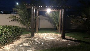 Eine terrasse mit steinbelag und einer hölzernen Pergola, umgeben von Grünpflanzen und Palmen.