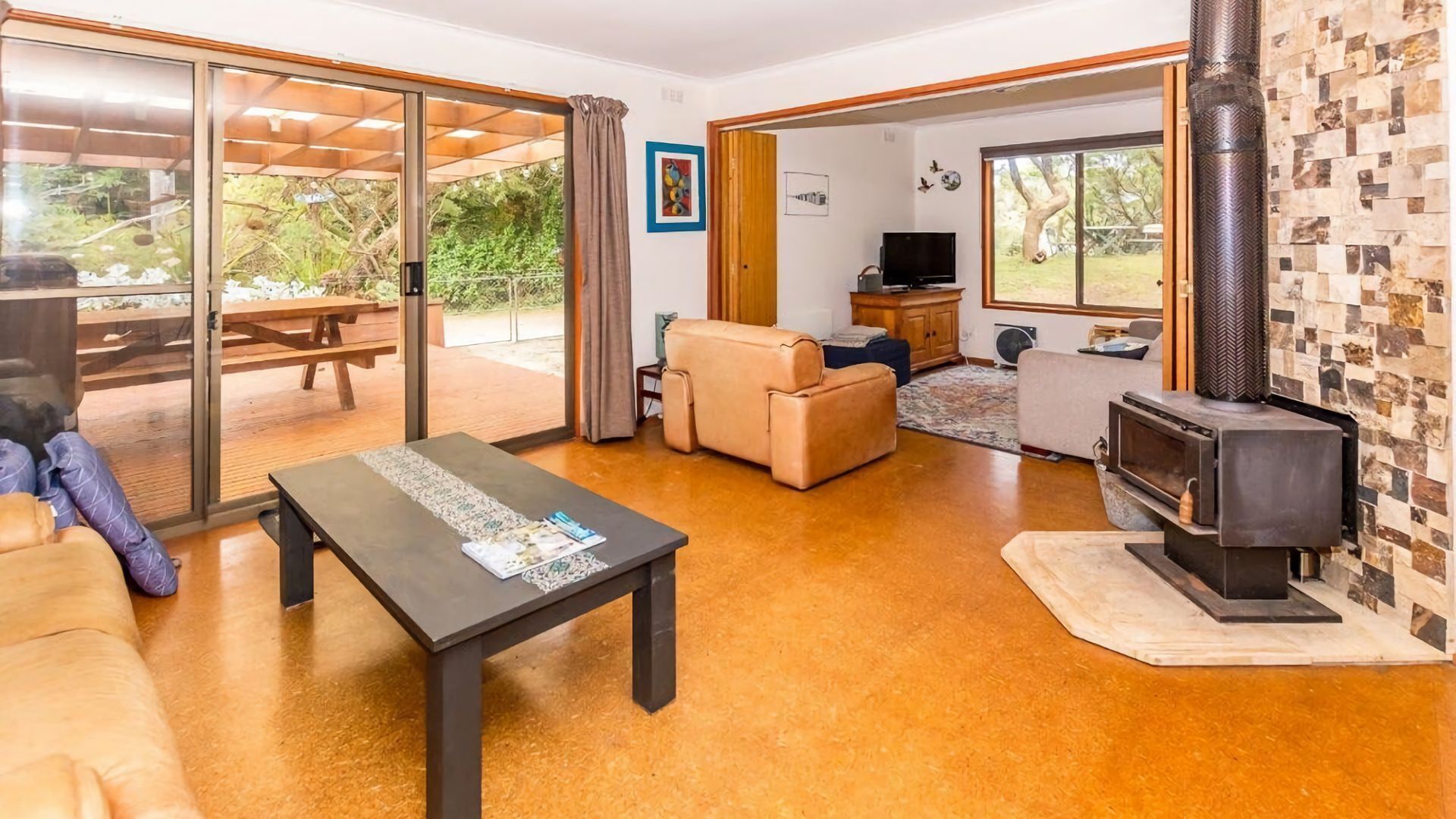 A spacious living room with a sofa, a coffee table, a fireplace, and a sliding glass door leading to an outdoor area with a picnic table.