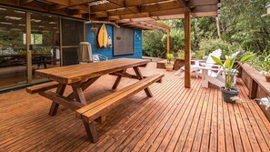 Une terrasse extérieure en bois, avec des tables de pique-nique et des plantes en pot.