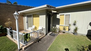 Une maison de plain-pied avec un patio couvert, un petit jardin et un mur en briques.