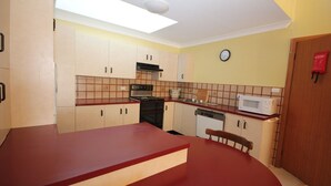 Une cuisine de taille réduite avec un plan de travail rouge, une cuisinière, un four à micro-ondes et un évier.