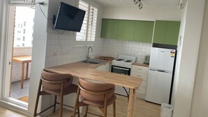 Una cocina moderna con una mesa de madera, dos taburetes de bar, horno empotrado, estufa y armarios verdes.