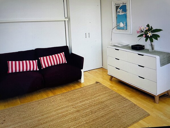 A modern living room with a dark sofa, striped pillows, a white dresser, and a small plant. - Studio 10 Bondi, roof top pool, walk to beach, air con, restaurants 2 mins (sydney)