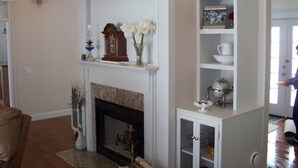 A living room with a fireplace, a white mantelpiece, and a built-in shelving unit. - Beautiful family retreat (Wayne)