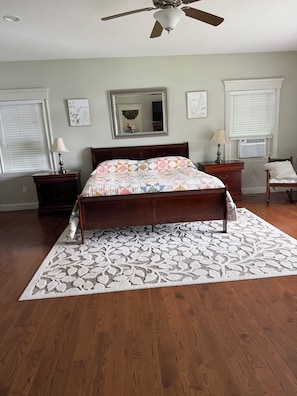 A bedroom with a wooden bed, a ceiling fan, a large mirror, and a window with blinds.