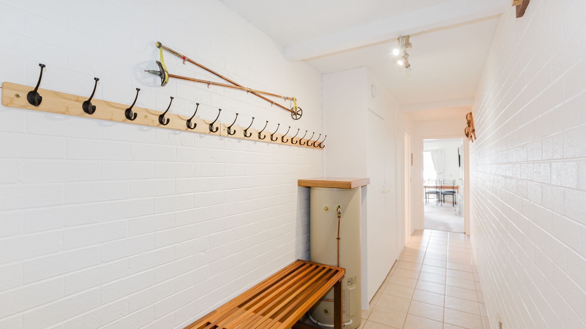 A hallway with a white brick wall, a wooden bench, and a row of hooks on the wall.