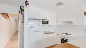 A modern kitchen with white cabinets, a microwave, a stove, and a refrigerator. - Central Park - 10/1 Snowy River Avenue (Jindabyne)
