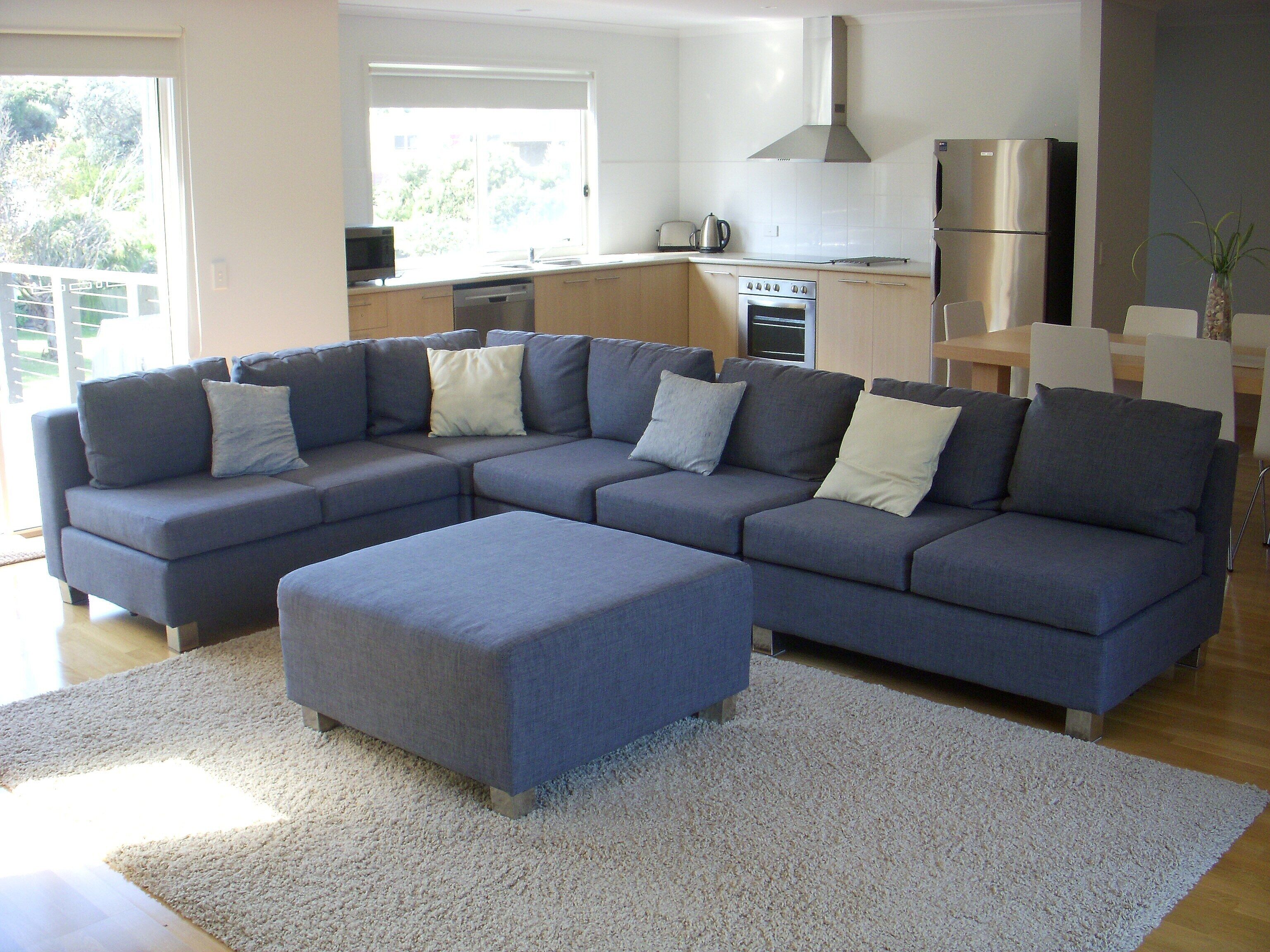 A modern living room with a sectional sofa, a dining area, and a kitchen with stainless steel appliances.