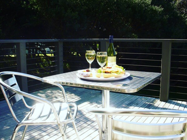 A table with a bottle of wine, two glasses, and a plate of food on an outdoor deck.