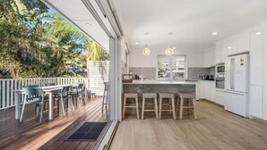 A modern kitchen with white cabinets, a wooden countertop, and a built-in oven. There is a deck with outdoor seating and a view of greenery.