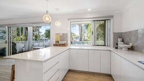 A modern kitchen with a large island, sliding glass doors to a balcony, and a view of the outdoors.
