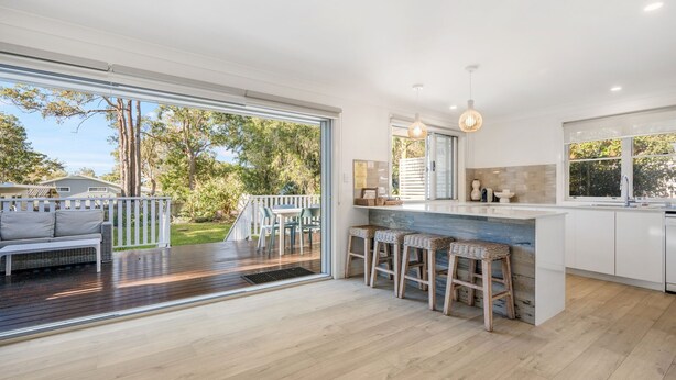 A modern kitchen with a large island, bar stools, and a view of the garden.