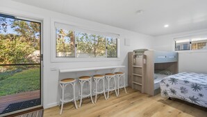 A bedroom with a bunk bed, a window with a view of trees, and a white bench with stools.