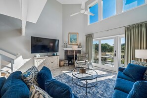 Una sala de estar moderna con sofá, televisor, chimenea y un balcón con cortinas.