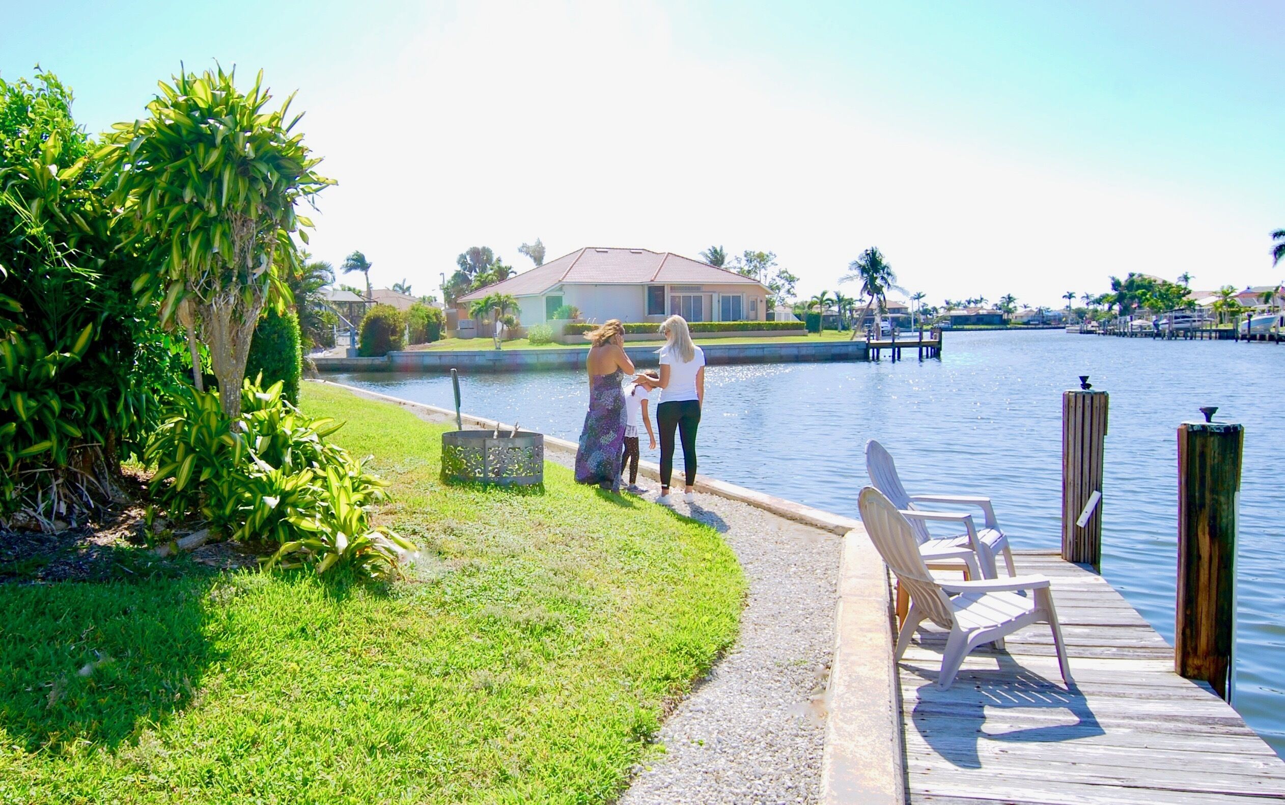 A wooden dock with chairs, a grassy area, and a body of water with a house in the background.