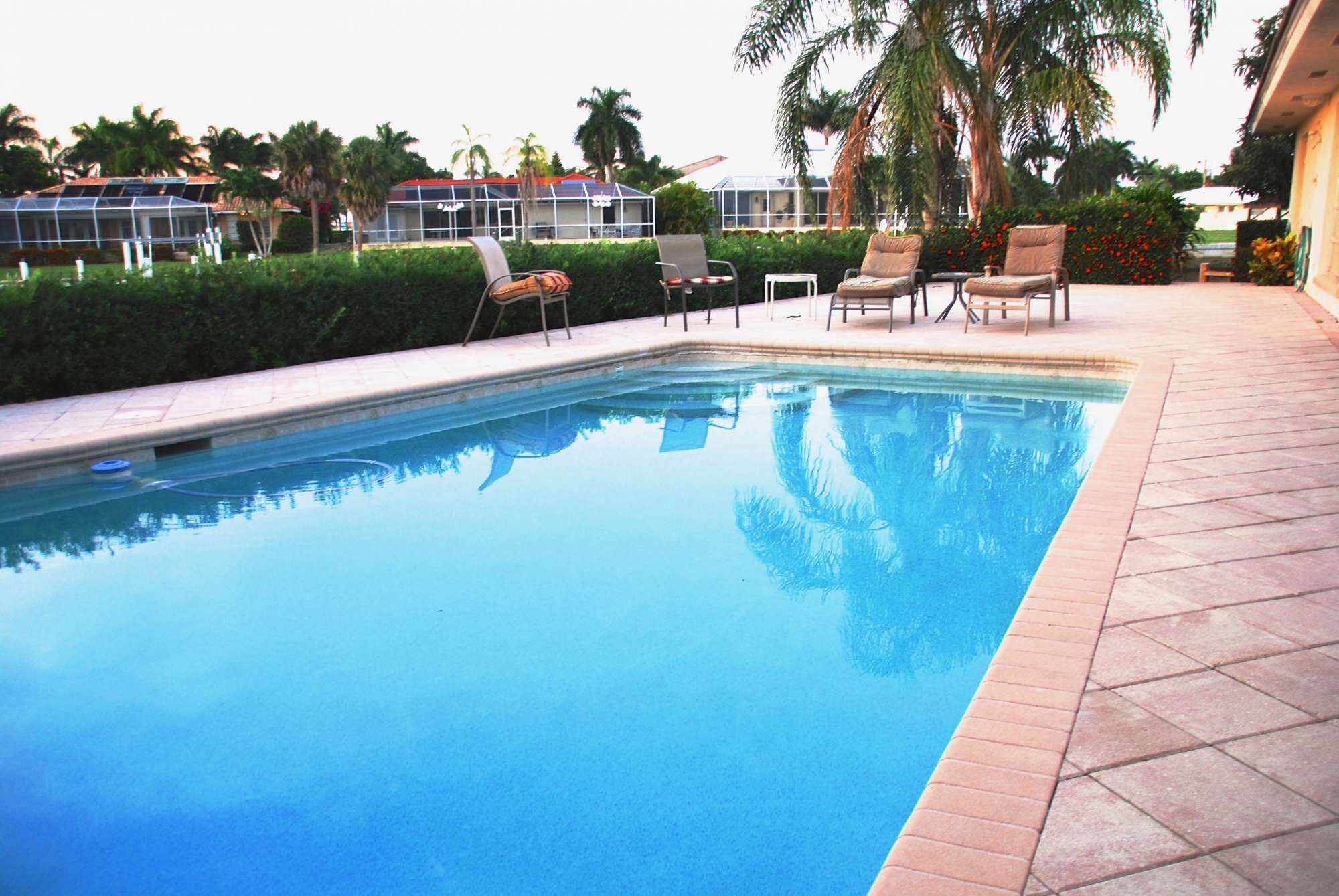 A swimming pool with a tiled edge, surrounded by lounge chairs and a hedge.