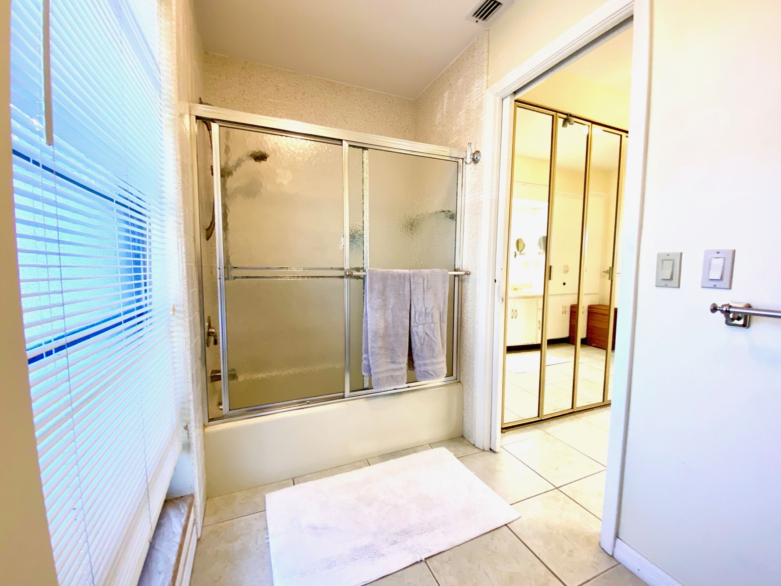 Un baño con cabina de ducha de vidrio, un perchero y una puerta blanca que da a otra habitación.