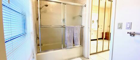 Un baño con cabina de ducha de vidrio, un perchero y una puerta blanca que da a otra habitación.