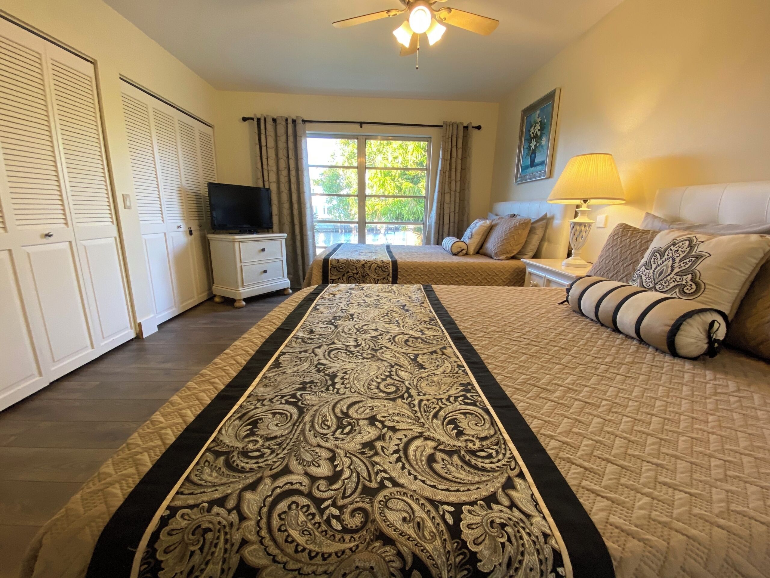 A hotel room with a large bed, a TV, a desk, and a window with curtains.