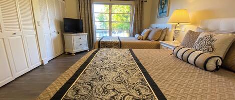 A hotel room with a large bed, a TV, a desk, and a window with curtains.