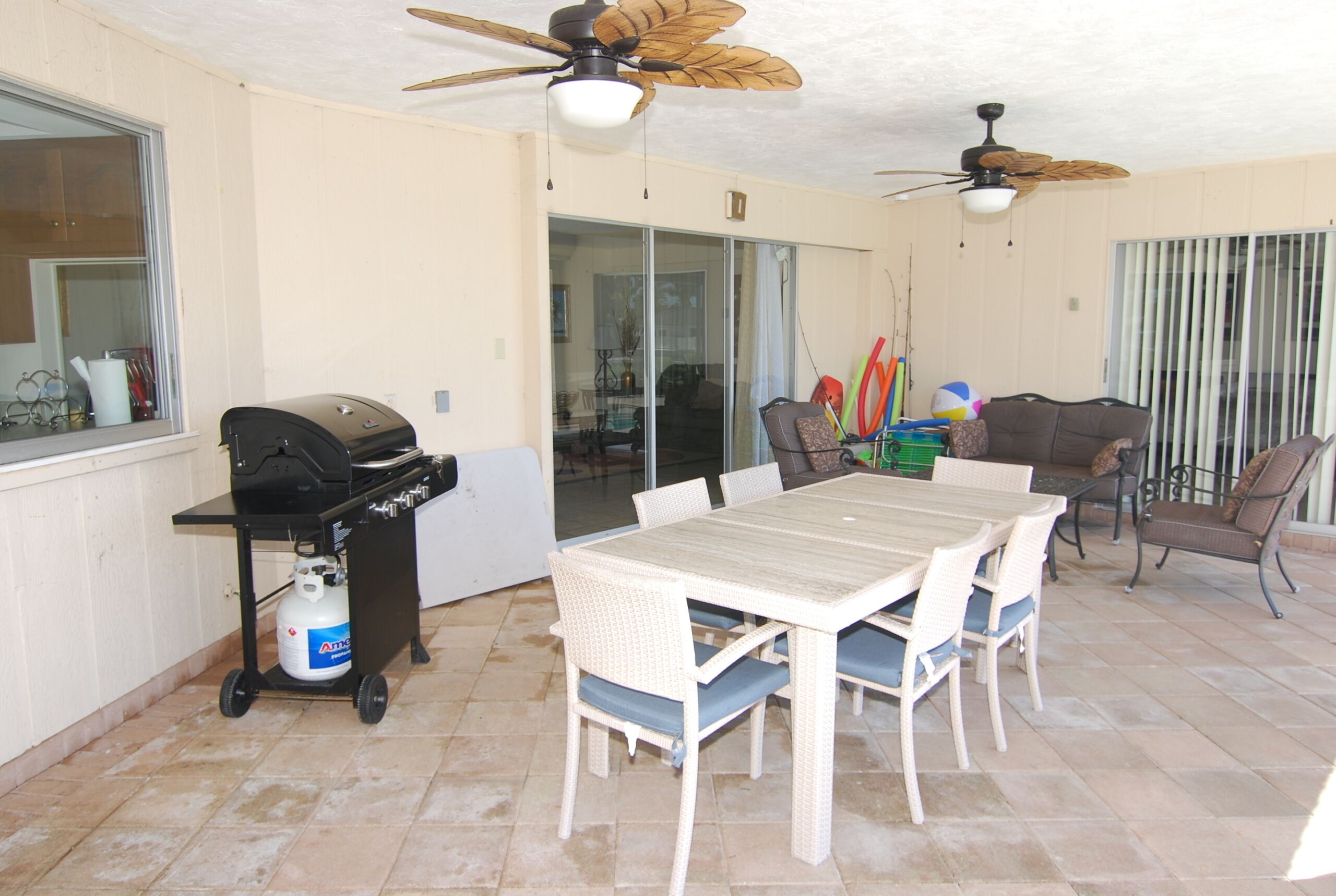 Un patio al aire libre con mesa y sillas, una parrilla y ventiladores de techo.