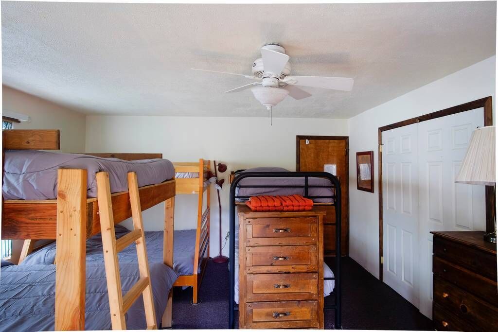 A dormitory room with bunk beds, a ceiling fan, a wooden dresser, and a door.