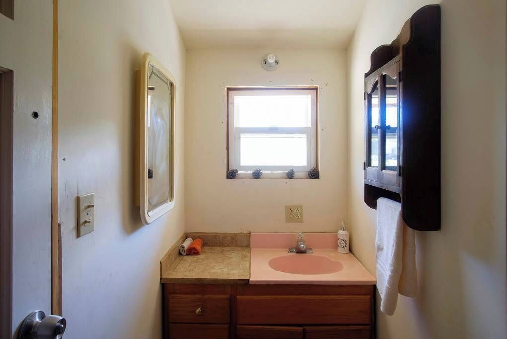 A small bathroom with a window, a sink, a mirror, and a towel rack.