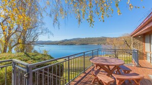 A wooden deck with a picnic table and benches overlooking a lake with a distant shoreline.