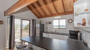 Eine moderne Küche mit einer großen Kochinsel, Holzbalkendecke, Blick durch das Fenster und einem kleinen Kühlschrank.