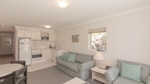 A compact living space with a kitchenette, a grey sofa, a small table, and a lamp. - Horizons - 505/10 Kosciuszko (Jindabyne)