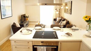 Eine moderne Küche mit einer zentralen Kochinsel, integriertem Backofen und einem Essbereich mit einer Couch und Tisch für zwei Personen.