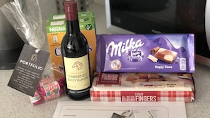 Eine Küchenarbeitsfläche mit einer Weinflasche, Nestlé-Milchkartons, Milka-Schokolade, Tesco-Shortbread-Fingern, einem Schlüssel und einer Gästeinformationskarte.