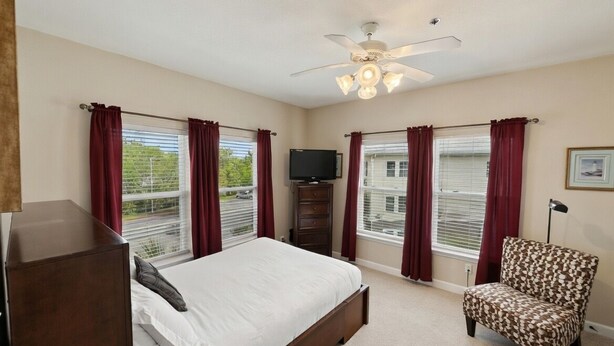 A bedroom with a bed, a chair, a ceiling fan, and a TV. - Waterfront Condo w/ Boat Docking & Fishing (Foley)