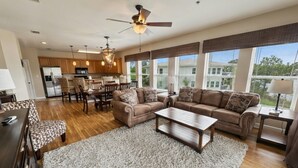 A spacious living room with a large sofa set, a coffee table, and a dining area with chairs and a table. - Waterfront Condo w/ Boat Docking & Fishing (Foley)