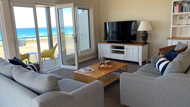 A living room with a TV, sofa, coffee table, and a view of the ocean through glass doors.