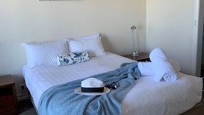 A neatly made bed with white linens, a blue floral pillow, a grey blanket, and a white towel.
