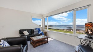 A living room with a view of the sea, a sofa, a coffee table, and a TV on a stand. - A Top Deck - vast views of the Southern Ocean (Port Fairy)