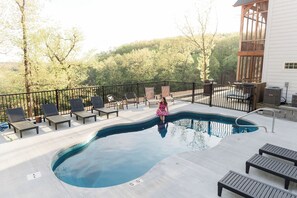 A swimming pool with lounge chairs and a wooden deck, surrounded by trees and a building.