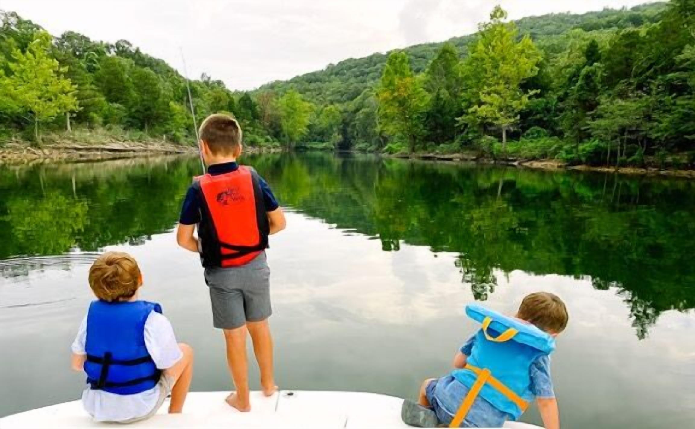 Trois enfants se trouvent dans un bateau, portant des gilets de sauvetage, et sont entourés d’un lac paisible et d’une végétation luxuriante.