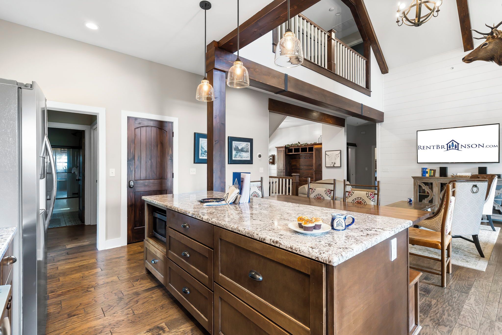 A spacious kitchen with a large island, wooden cabinetry, and a dining area with a high ceiling and exposed beams.